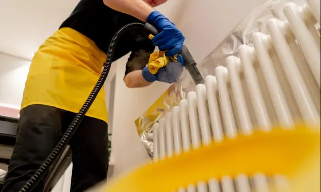 Cleaner steam cleaning a radiator to remove built up dust