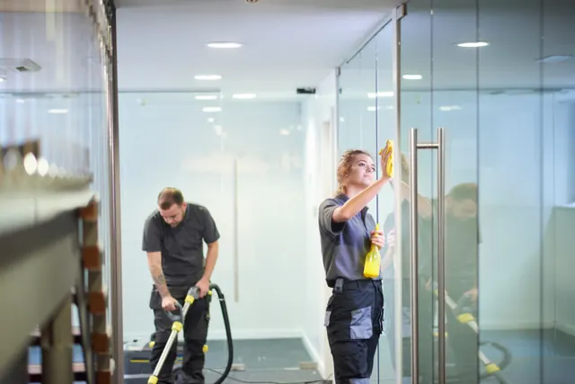Commercial cleaning team vacuuming and wiping glass in an office
