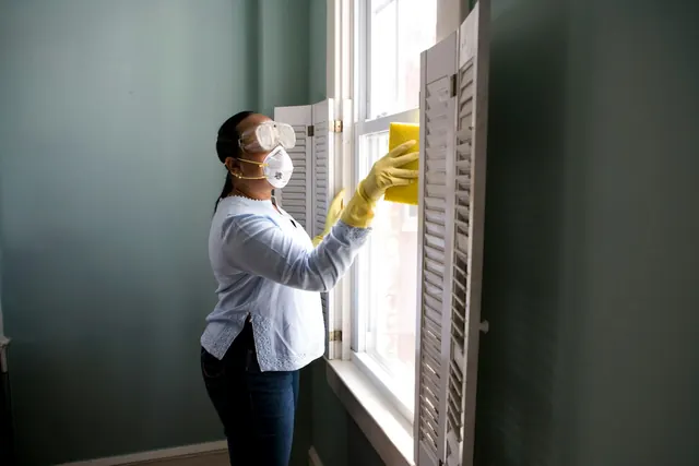 Professional cleaner in a mask wiping down a window frame
